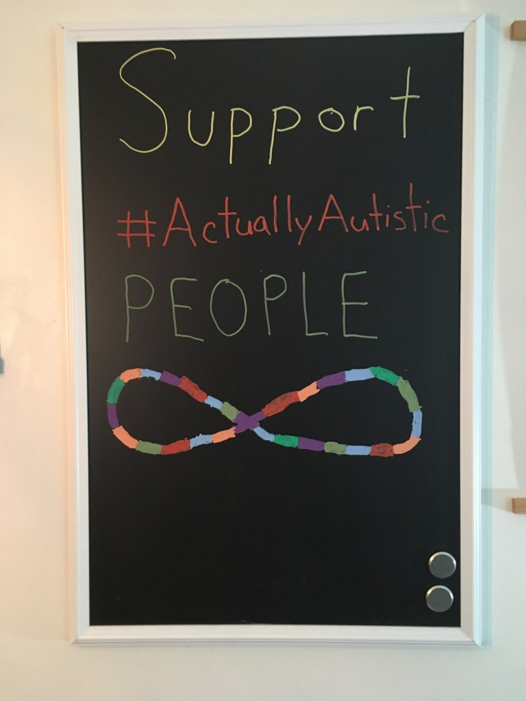 Image Description: Photo of a blackboard that says "Support #ActuallyAutistic People" with a multicoloured infinity symbol at the bottom