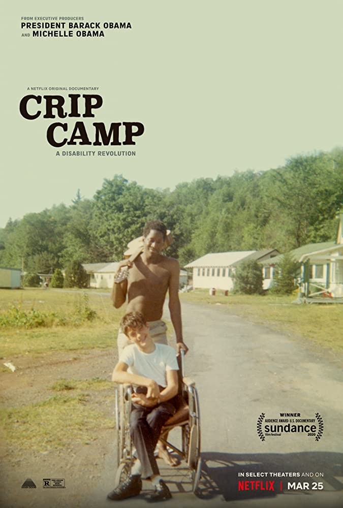 Image Description: Poster for the Netflix Documentary Crip Camp. The Title is in white in the upper left corner. In the background are  white buildings in the foreground a shirtless black man leans a guitar over his right shoulder while pushing a white young man wearing trousers and a white shirt in his wheelchair
