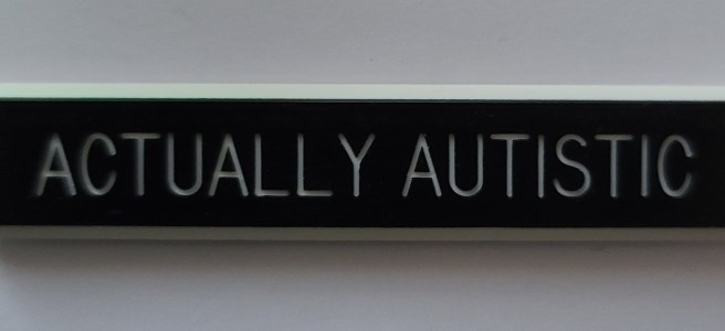 Image Description: Black Label with White writing that says "Actually Autistic"